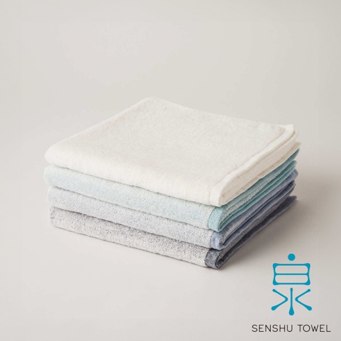 YUKINONE 雪之音柔織有機棉浴巾疊放展示，包含白色、淺藍、藍色和深藍色四種顏色。浴巾材質柔軟，織紋細緻，角落處有品牌標誌。