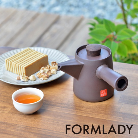 日製萬古燒紫砂橫手急須茶壺，呈現深棕色，壺蓋為木質，壺身有紅色印章。茶壺置於木桌上，旁有一盤切塊點心、堅果及一小杯茶。