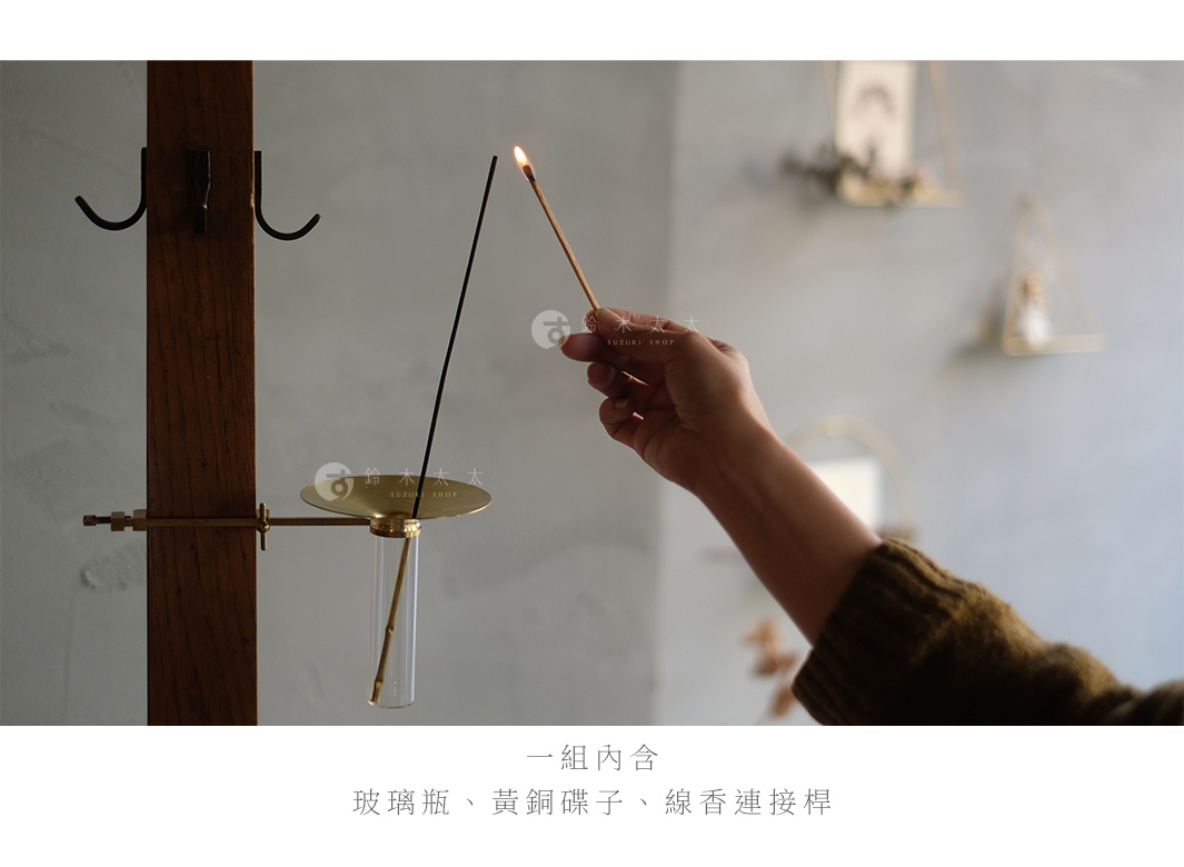 黃銅可夾式玻璃線香架，一端固定於木架上，包含一個圓形黃銅盤、一支透明玻璃管，以及一根燃燒中的細長線香，另一端由手持。