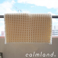 米白色七層紗拭巾，織有小格子紋理，邊緣有流蘇，掛在欄杆上，背景為藍天白雲與建築。