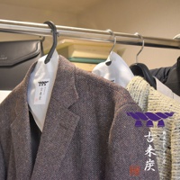 兩件斜紋軟呢夾克掛在衣架上，其中一件夾克有標示「古來炭」字樣的白色調濕紙，另件夾克則有紫色繩結圖案和「古來炭」日文標示。