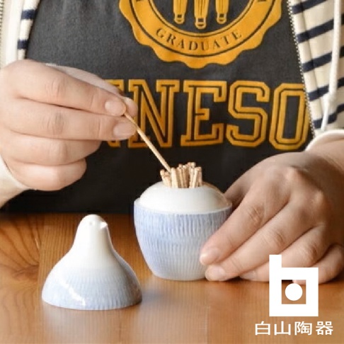 陶瓷牙籤瓶，瓶身有藍色條紋，瓶蓋為白色鳥造型，牙籤瓶內裝有牙籤，由雙手操作。
