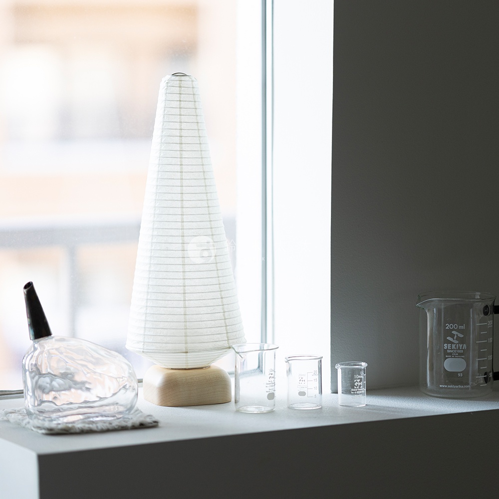 一個錐形白色紙質迷你裝飾提燈，帶有細綠色條紋，立於木製底座上。提燈旁有兩個小型透明玻璃燒杯和一個較大的透明玻璃燒杯，其上印有刻度和品牌標識。
