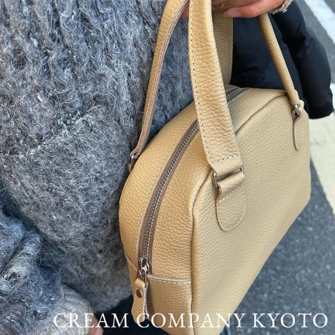 一隻淺駝色荔枝紋皮革迷你手提包，包身呈半月形，配有拉鍊開合及一對短提把。