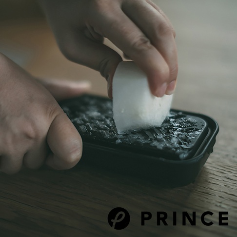 一雙手正在使用黑色兩用盒上的磨泥器，將白色塊狀物磨成細碎狀，盒內已有多量磨碎的細末。