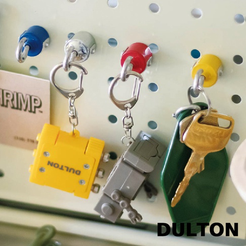 DULTON 品牌字樣下方，懸掛著四個造型各異的鑰匙圈，分別是藍色、銀色、紅色和黃色的磁吸掛勾，其中黃色掛勾旁還有一個綠色的鑰匙套。