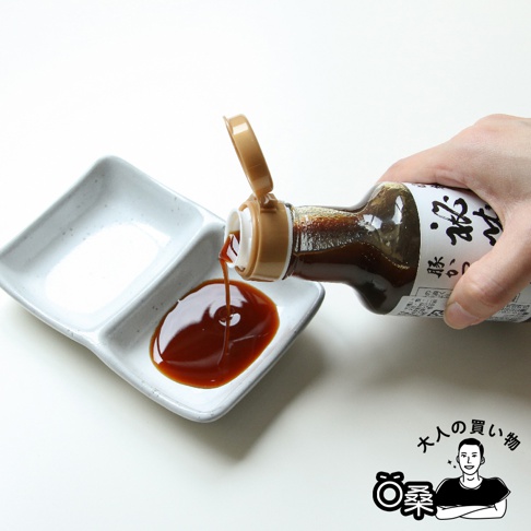 一隻手拿著塑膠瓶，將深棕色的秘藏豬排沾醬，倒進一個白色雙格小碟子裡。