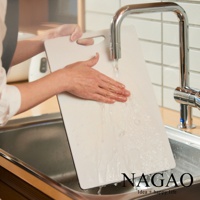 一隻手正在水龍頭下清洗一個白色的雙面抗菌耐熱砧板，砧板置於廚房水槽上方。