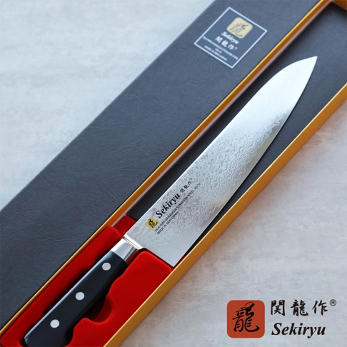 VG10不鏽鋼33層大馬士革紋路牛刀，刀刃長24公分，黑色握柄，置於黑色包裝盒內的紅色絨布刀架上。