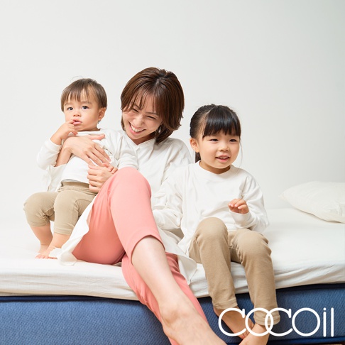 一位母親和兩名兒童坐在藍色床墊上，床墊表面為白色，有乳膠材質的感覺。