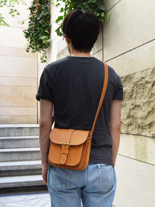 棕褐色皮革製成的單肩包，具有十字繡細節和金屬扣環，由一個人斜挎著。