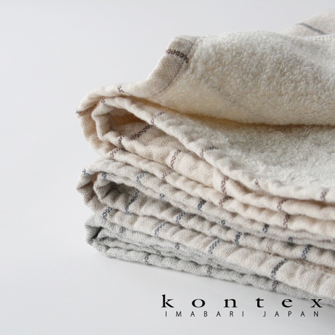 一疊有機棉浴巾，表面有細緻的格紋織紋，顏色為米白與淺灰色，材質觸感柔軟。