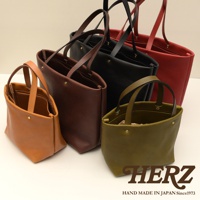 職人手作皮革托特包，展示多種顏色，包含駝色、深棕色、黑色、紅色及橄欖綠。包款設計簡約，以皮革材質製作，具有雙提把及四個內袋，適合日常攜帶。