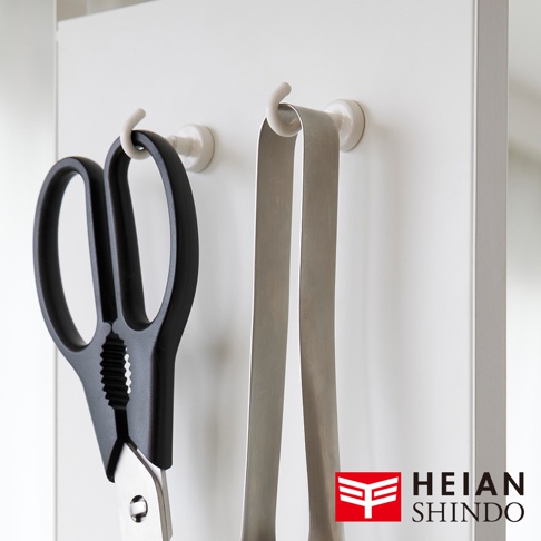 模式B： 一款黑色手柄的剪刀和一個金屬夾子掛在白色的牆壁掛鉤上，旁邊是 HEIAN SHINDO 的品牌標誌。