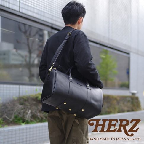 一個男人身背黑色皮革波士頓包，包上有金色鉚釘和可調節肩帶。