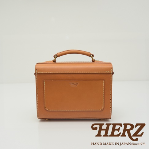 職人手作皮革極簡風兩用迷你單肩包，採用 tan 色皮革製作，包身結構方正，配有頂部提把及金屬釦環，正面設有方形插袋，邊緣以對比色縫線裝飾，展現細緻工藝。