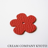 紅色皮革製成的五瓣花形吊飾，表面有細緻紋路，中心有圓形孔洞，可作為京都職人手作隨身手機包的配件。