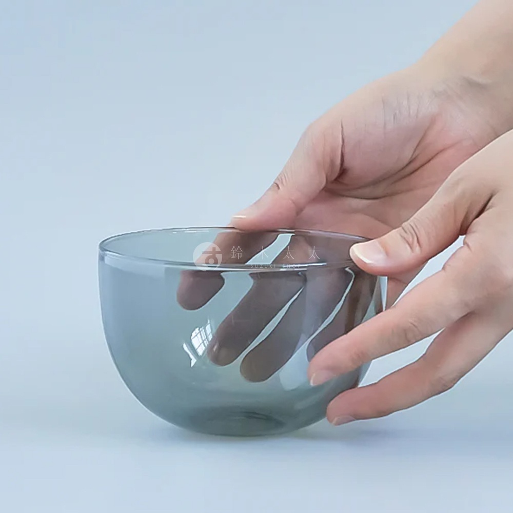 一隻手捧著一只淺灰色、半透明的玻璃點心碗，碗身圓潤，邊緣光滑。