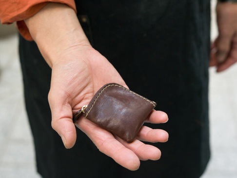 職人手作的咖啡色皮革零錢包，方形設計，有黃銅色拉鍊，縫線細緻，以手持展示。