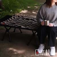 日本桃雪戶外格紋棉柔浴巾，上面鋪在黑色摺疊床架上，有人手持金屬杯坐在床邊。