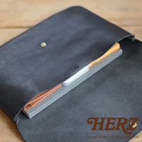 黑色皮革製成、帶有鈕扣的長方形小物收納袋，內部可見一疊筆記本和手機，材質為真皮。