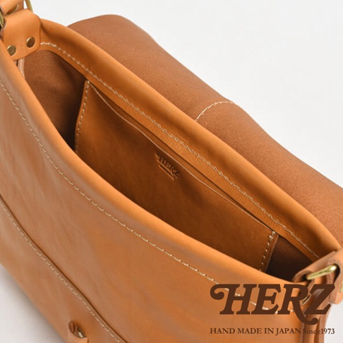 HERZ 品牌商標和 HAND MADE IN JAPAN Since 1973 字樣，呈現一個職人手作皮革包內部的特寫，可見縫線和皮革紋理。