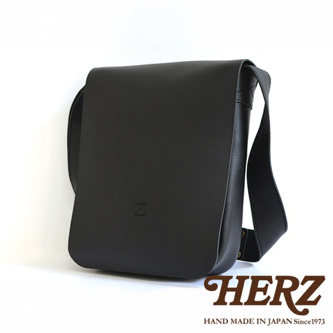 一個黑色皮革軟皮直式斜背包，上面印有「Z」字樣，底部有「HERZ HAND MADE IN JAPAN Since1973」的品牌標誌