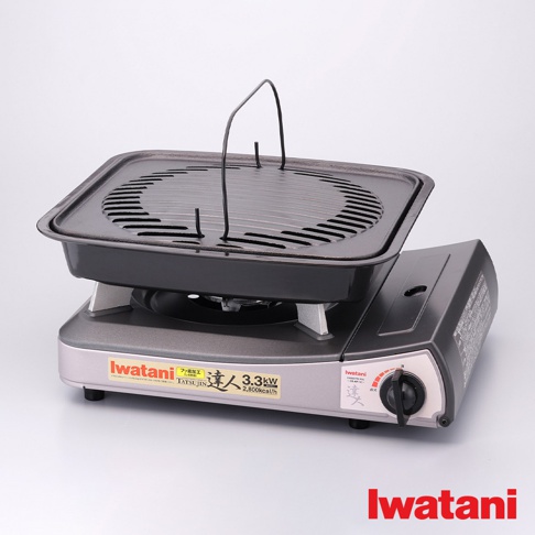 卡式爐專用鑄鐵烤盤，黑色烤盤上方設有金屬提把，烤盤表面為條紋狀，底部有銀色支架，置於灰色卡式爐上，卡式爐側面有黑色旋鈕及標誌。