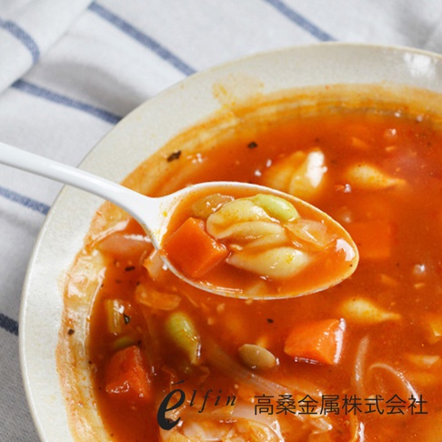 日製白色琺瑯餐匙，盛著一勺番茄湯，湯內有義大利麵疙瘩、紅蘿蔔塊、豆子和洋蔥。