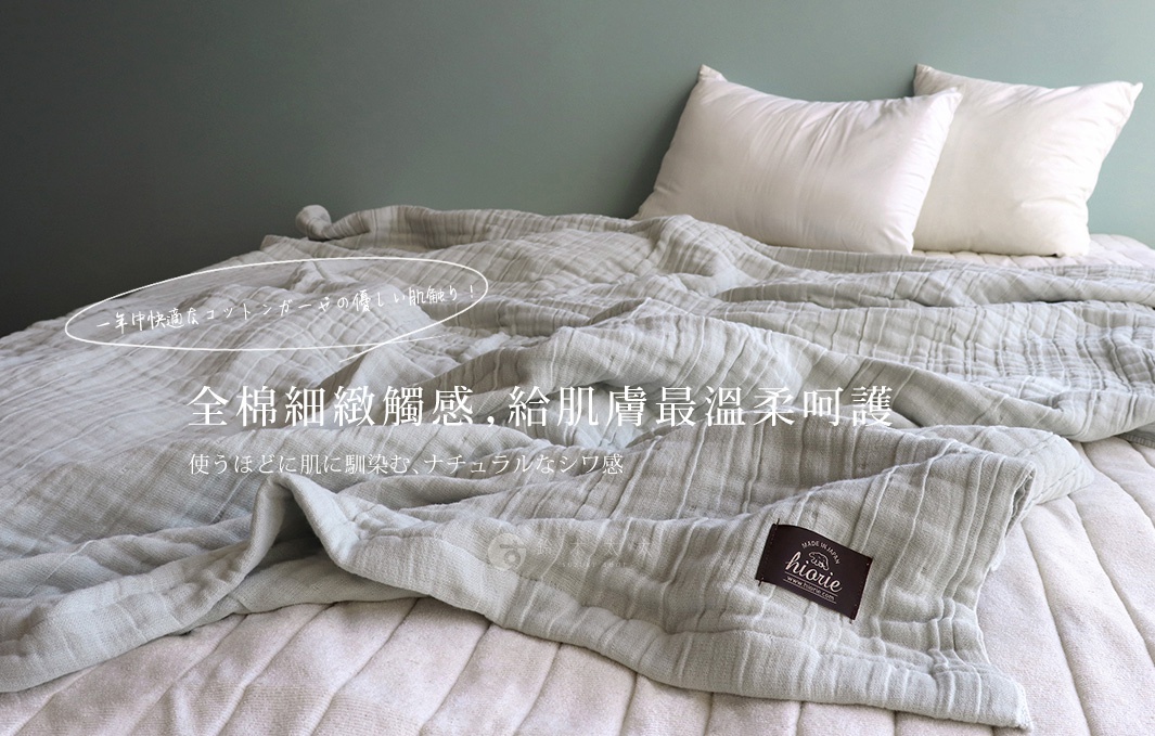 一件淺灰色八層紗雙人被，材質為全棉，質地柔軟，帶有自然的皺褶感。被子平鋪在床鋪上，背景有兩個白色枕頭。