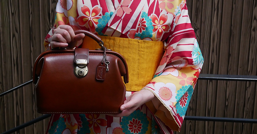 棕色皮革迷你醫生包，帶有金色旋轉鎖扣和鑰匙吊飾，由穿著印花和服的人士手持。
