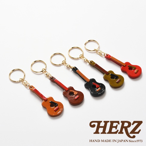 五款職人手作皮革吉他造型鑰匙圈，分別為橘色、紅棕色、黑色、橄欖綠及紅色，皆配有金色鑰匙圈，展現精緻細膩的手工藝。