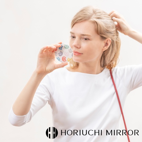 女性手持圓形隨身化妝鏡，鏡面印有粉、藍、黃、紫等色系的可愛貓咪頭像圖案，鏡框為白色。