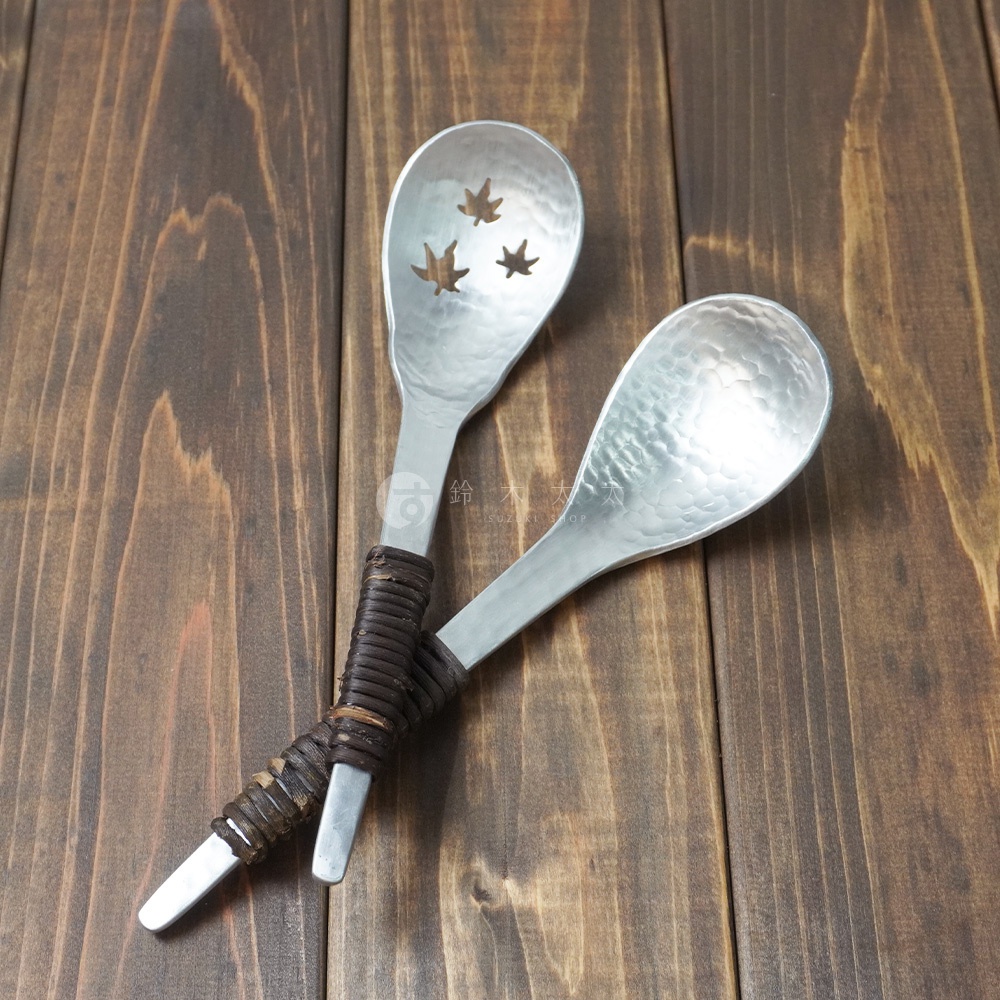 兩支鋁製瀝水湯勺，勺面有錘目紋，其中一支勺頭有三片鏤空楓葉圖案，握柄處纏繞著咖啡色皮革。