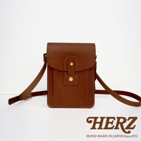 棕色皮革製成的直立式斜背包，正面有兩個金屬釦和縫線裝飾，附有可調整的長背帶。