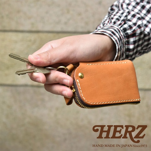 職人手作皮革鑰匙包，採用天然皮革材質，呈現溫潤的棕褐色。包體設有拉鍊開合，並附有鑰匙圈，方便收納與攜帶鑰匙。