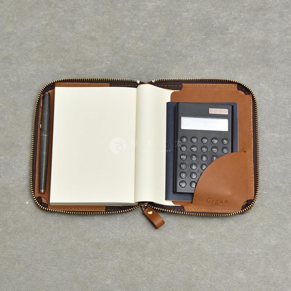 一個打開的棕色皮革記事本收納包，裡面有一個空白筆記本、一支筆和一個黑色計算機。