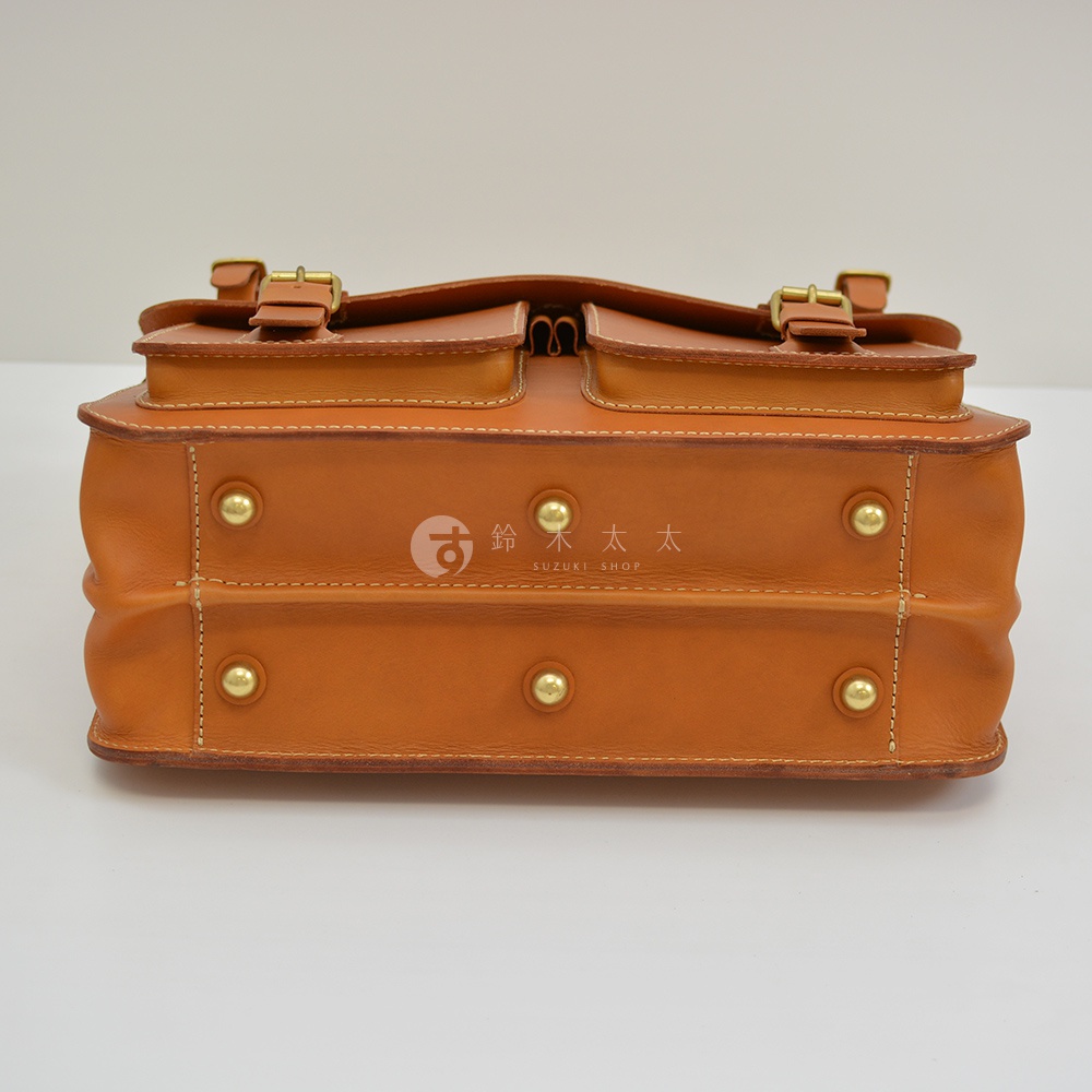 職人手作皮革旅行包 A-102，咖色，採用真皮材質，正面有兩個翻蓋口袋，並以黃銅釦具及鉚釘固定，包身側面有明顯的縫線與皮革紋理。