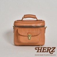 職人手作的淺棕色皮革相機包，圓潤的包身設計，頂部有提把，正面有一個翻蓋式小口袋，附有金色金屬鎖扣，整體呈現簡約復古風格。