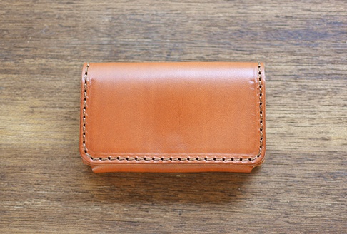 棕色皮革名片夾，縫線精緻，風格簡約，置於木紋背景上。
