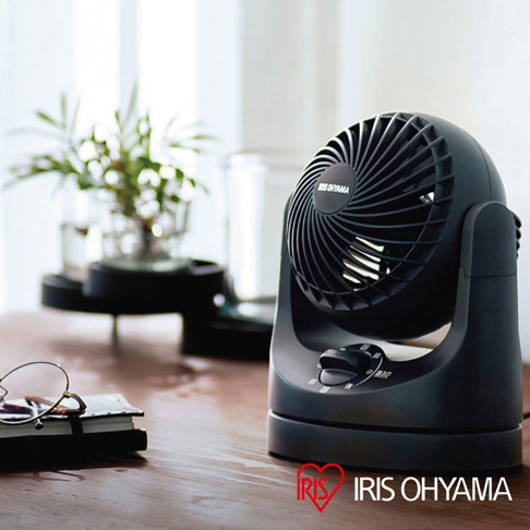 黑色極靜音迷你型空氣循環扇，扇葉紋路清晰，機身圓潤，設有黑色旋鈕調速鍵，放置於木質桌面，一旁有眼鏡和筆記本，背景為綠植與窗戶。