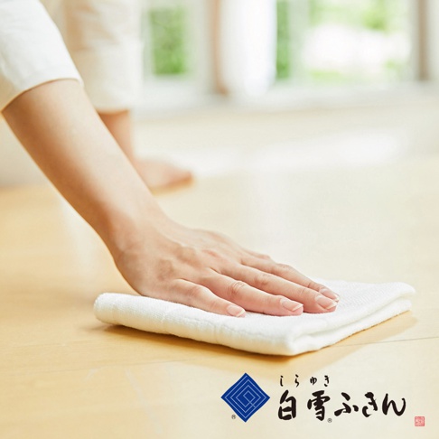 一隻手正用一條白色木纖維拭巾擦拭木質地板。