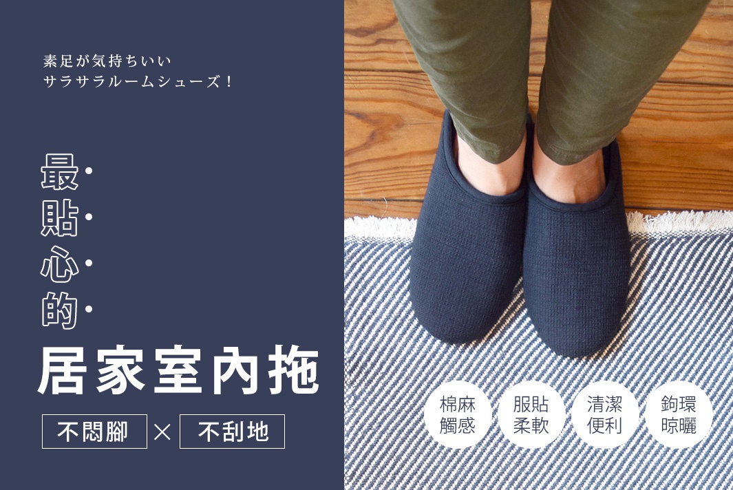 一雙深藍色棉麻材質的居家室內拖鞋，鞋面有細緻的織紋，套腳式設計，穿著者穿著橄欖綠長褲，踩在藍白條紋地毯上。