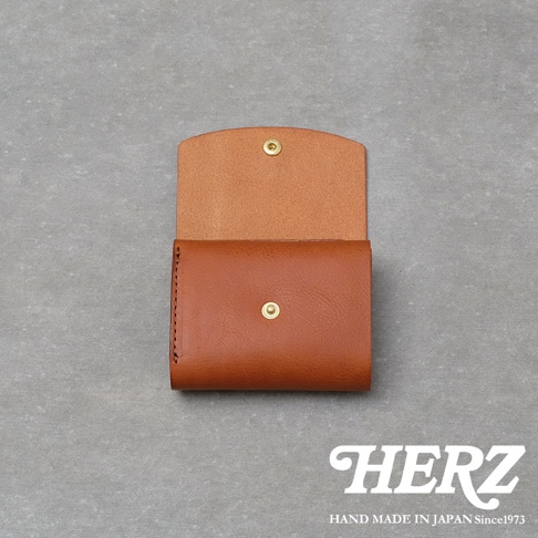 日本HERZ職人手作皮革迷你短夾，選用棕色Minerva Box皮革製成，正面中央帶有金屬壓扣設計，翻蓋打開後呈現內部原皮色澤與結構，整體展現簡約質感與日本手作工藝。