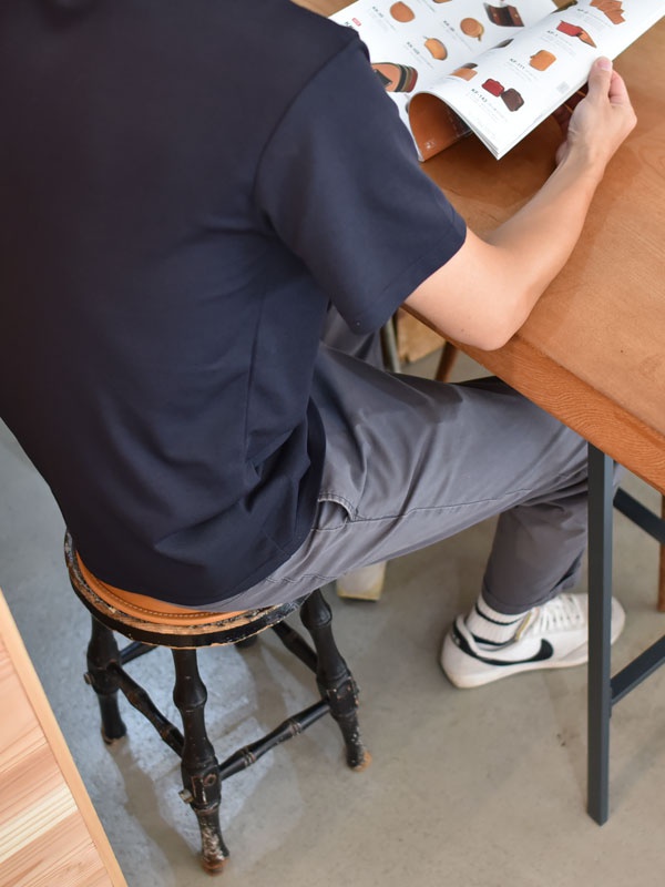 黑色木質四腳凳，圓形棕色皮革坐墊，頂部邊緣有縫線細節。