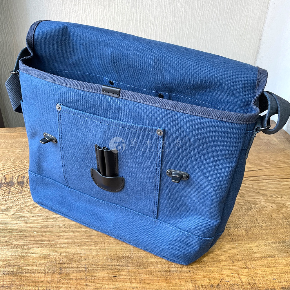 藍色純棉帆布雙扣郵差包，有前袋和翻蓋設計。