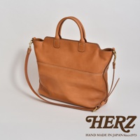 職人手作皮革兩用托特包，呈現自然棕色調，包身線條簡約，雙提把設計，配有可拆卸斜背帶，精緻車縫線展現皮革質感。