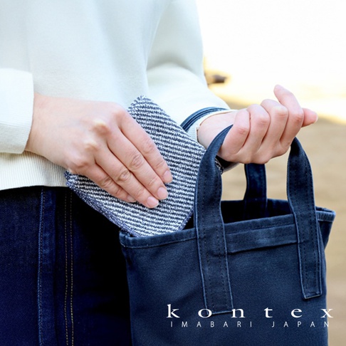 手持一塊藍白條紋、織紋明顯的方巾，正在放入一個深藍色帆布托特包。
