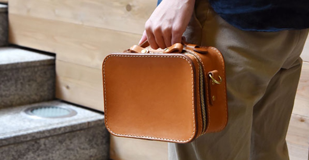 HERZ 品牌職人手作皮革兩用迷你小方包，棕褐色硬皮革材質，附有拉鍊開合及提把。
