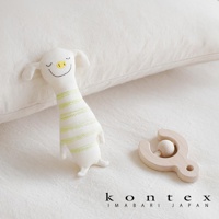 白色有機棉抓握玩偶，帶有綠色條紋，造型像可愛的動物，臉部有黑色線條繡出的眼睛和嘴巴，黃色鼻子。旁邊有一個淺木色的木製搖鈴。